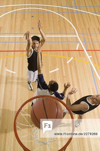 Ein Basketballspieler schießt einen Korb und zwei weitere Spieler spielen Verteidigung.