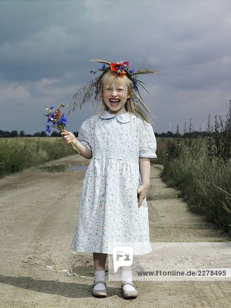 Ein Mädchen  das auf einer Landstraße steht und Wildblumen hält.