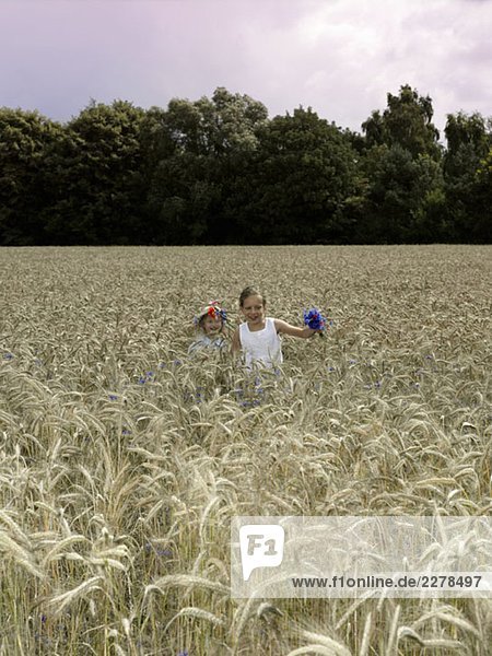 Zwei Mädchen  die durch ein Weizenfeld laufen.