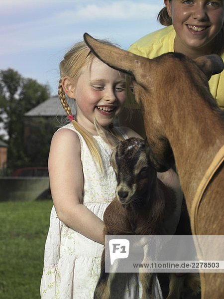 Zwei Mädchen mit einer Ziege und ihrem Kind.
