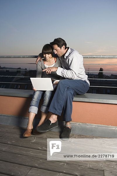 Ein Paar mit einem Laptop auf einer Dachterrasse