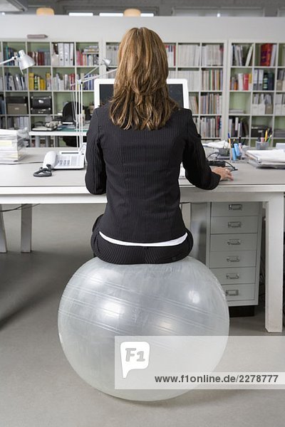 Eine Frau sitzt auf einem Übungsball an einem Schreibtisch in einem Büro.