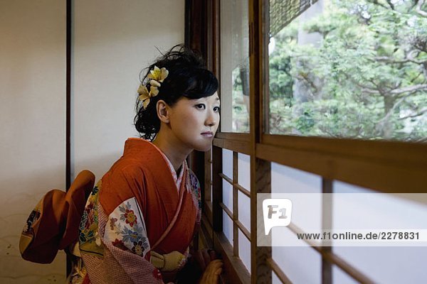 Eine Frau  die einen Kimono trägt und aus dem Fenster schaut.