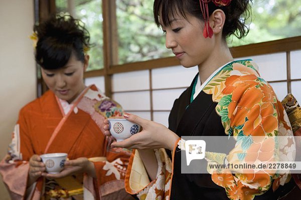 Zwei Frauen tragen Kimonos und trinken Tee.
