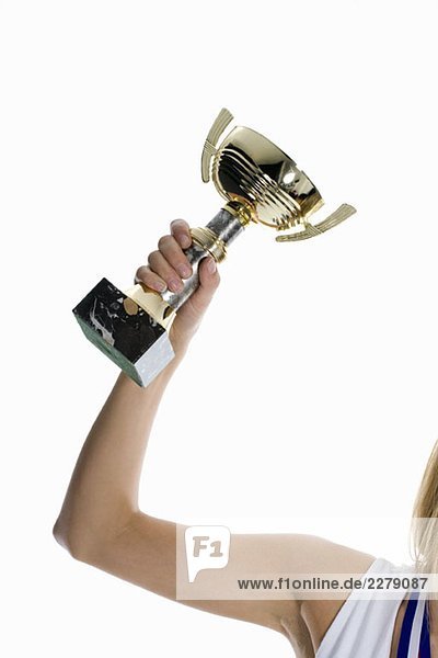 Der Arm einer Sportlerin hält eine Siegertrophäe hoch.