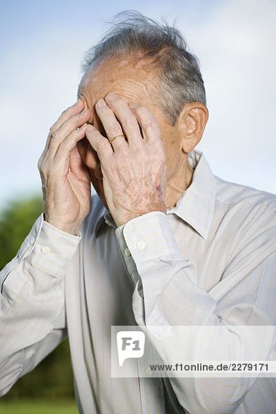 A senior man covering his face with his hands