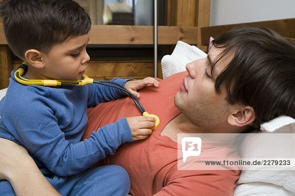 Ein Junge  der mit seinem Vater mit einem Spielzeug-Stethoskop spielt.