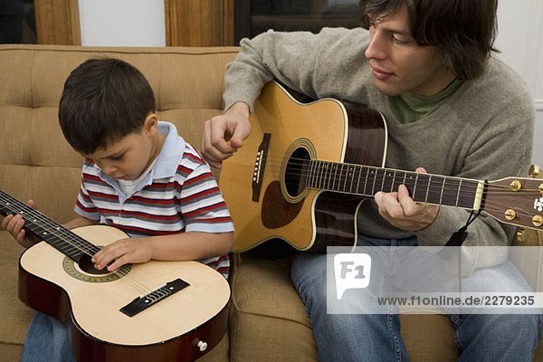 Ein Mann und ein Junge spielen zusammen Gitarre.