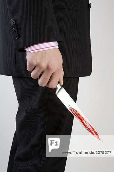 Ein Geschäftsmann hält ein Messer mit Blut darauf.