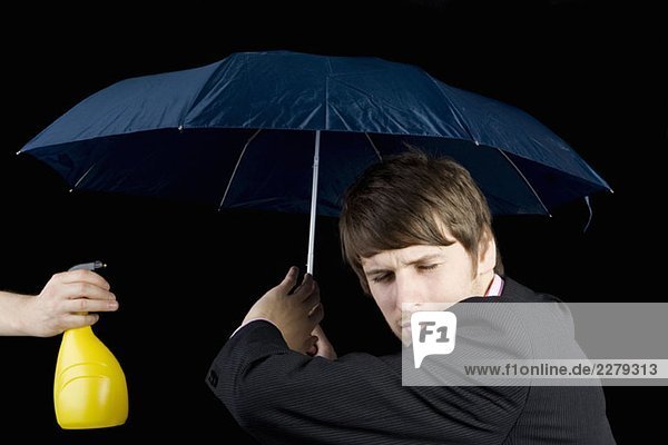 Ein Mann  der aus einer Wasserflasche gespritzt wird und einen Regenschirm hält.