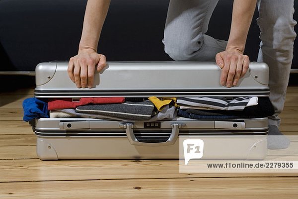 A person trying to close a suitcase