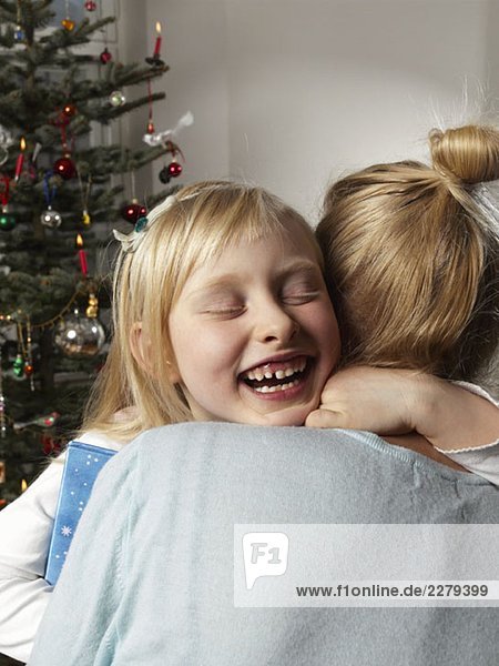 Ein Mädchen  das eine Frau neben einem Weihnachtsbaum umarmt.