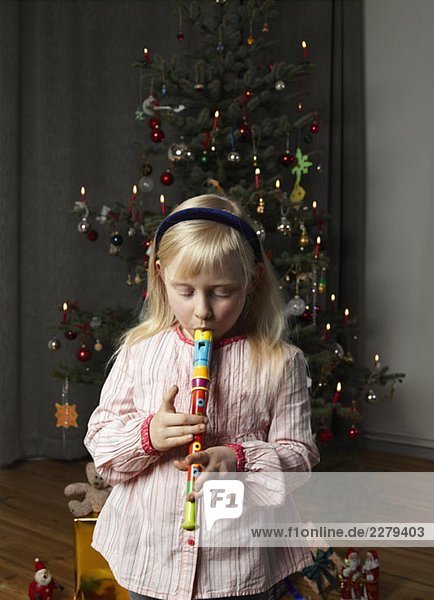 A girl playing a recorder in front of a Christmas tree