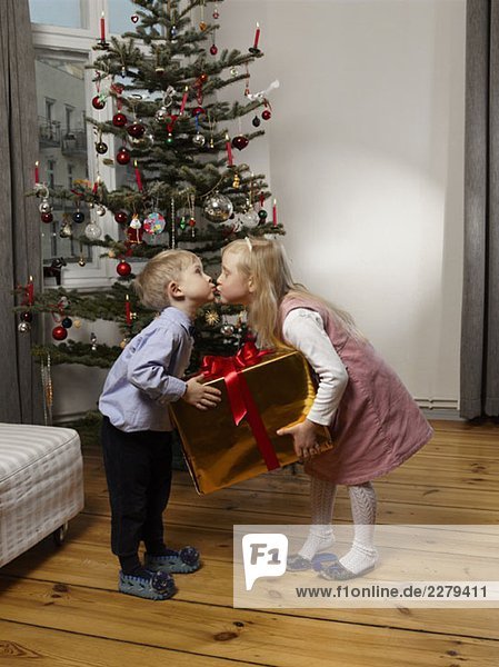 Zwei Kinder küssen sich vor einem Weihnachtsbaum