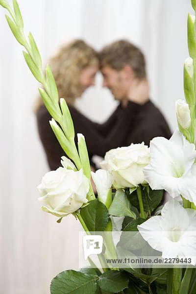 Ein Paar  das sich hinter einem Strauß weißer Schwertlilien und Rosen umarmt.