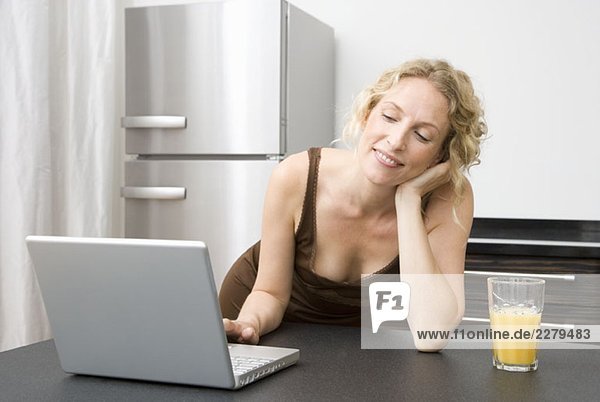 Eine erwachsene Frau  die sich mit einem Laptop auf eine Küchenzeile stützt.