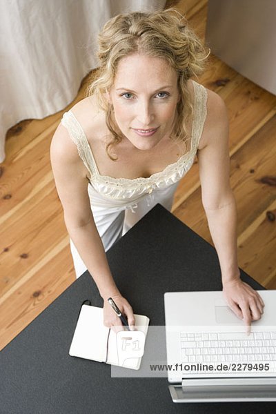 Eine Frau  die in ein Notizbuch schreibt und einen Laptop benutzt.