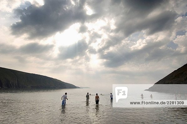 Gruppe der jungen Männer und Frauen stehen und Schwimmen im Meer an der Mwnt Bay westlich der Stadt Wales UK Cardigan. Die Bucht und die umliegenden Felsen sind im Besitz des National Trust