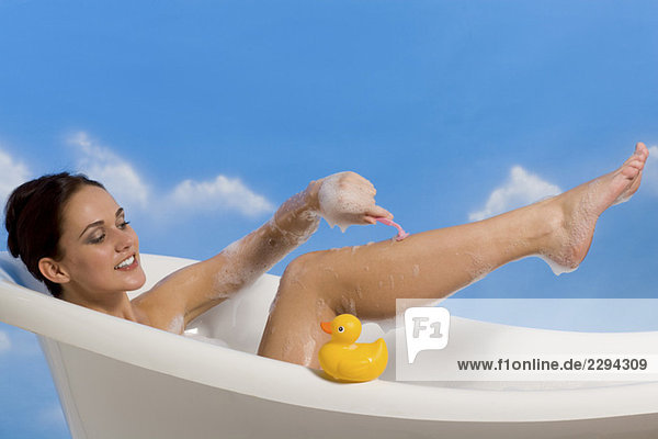 Junge Frau rasiert Beine im Bad