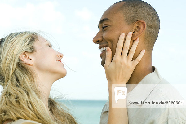 Couple smiling at each other  woman's hand on man's cheek  side view