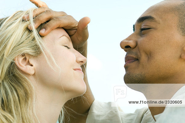 Man placing hand on woman's forehead  both with eyes closed  side view