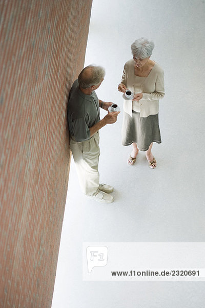 Couple standing face to face  both holding coffee cups  high angle view