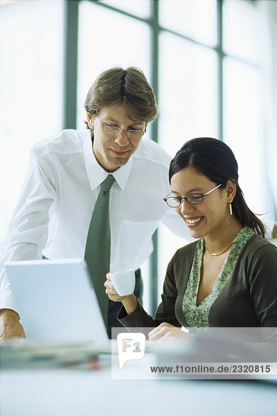 Male and female colleagues looking at laptop computer together  woman holding coffee cup