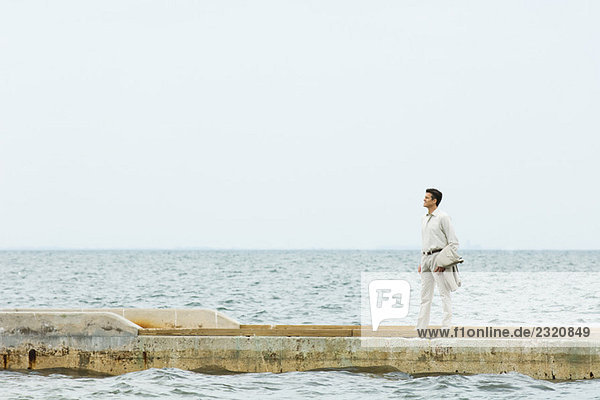 Mann auf Steg stehend  auf das Meer schauend  in mittlerer Entfernung