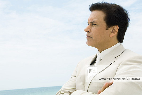 Businessman crossing arms  looking at distance  sea in background