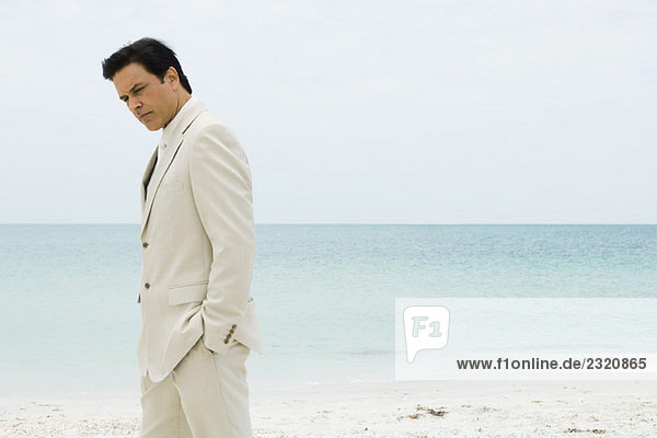 Geschäftsmann am Strand stehend mit Händen in den Taschen  nach unten schauend