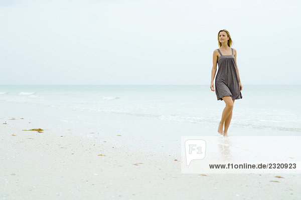 Frau im Sonnenkleid am Strand spazieren gehen  wegschauen
