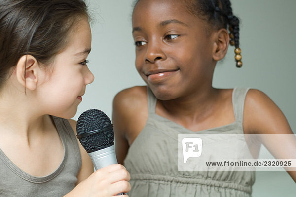 Two little girls smiling at each other  one holding microphone  close-up