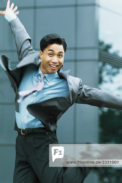 Businessman jumping in the air  arms out  smiling at camera