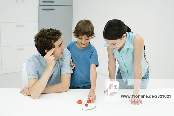 Father and two children in kitchen  making smiley face out of vegetables