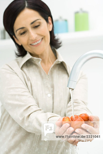 Frau hebt eine Handvoll Tomaten unter dem Wasserhahn auf  lächelnd