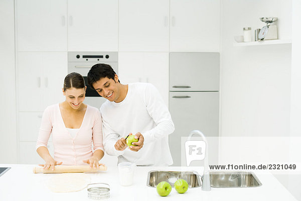 Paar steht zusammen an der Küchentheke  Frau rollt Teig aus  Mann schält den Apfel