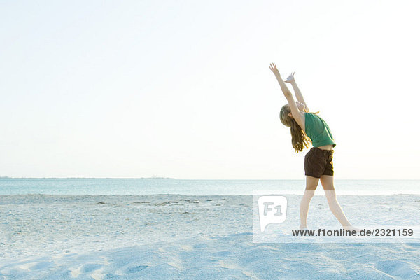 Kleines Mädchen am Strand stehend mit erhobenen Armen  Kopf zurück  volle Länge