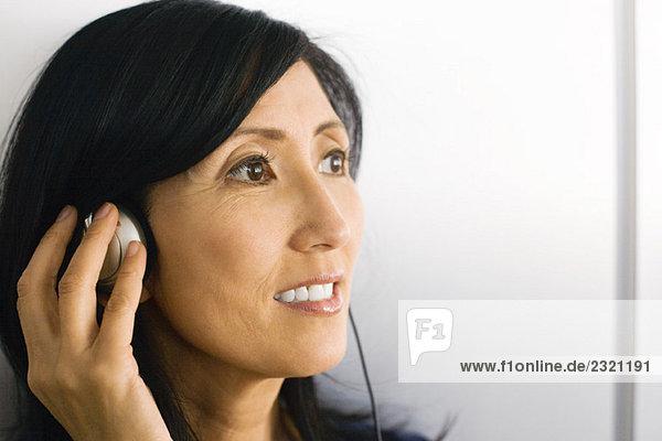 Woman listening to headphones  hand over ear  smiling  looking away