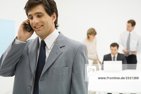 Businessman using cell phone  smiling  colleagues in background