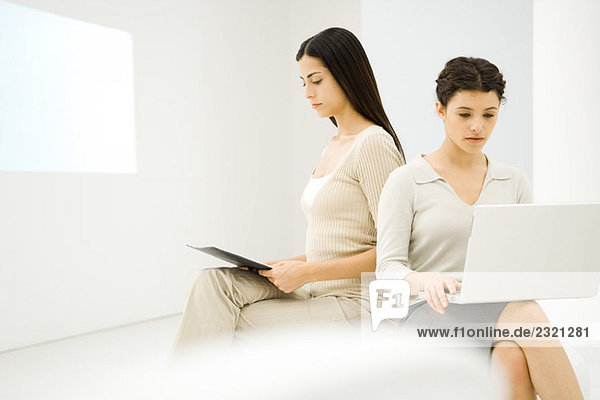 Zwei Geschäftsfrauen sitzen zusammen  eine mit Laptop-Computer  die andere mit Blick auf Dokument