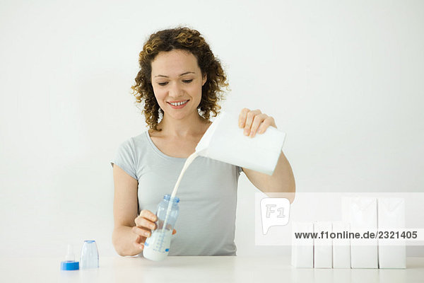 Frau gießt Milch aus dem Karton in die Babyflasche  lächelnd