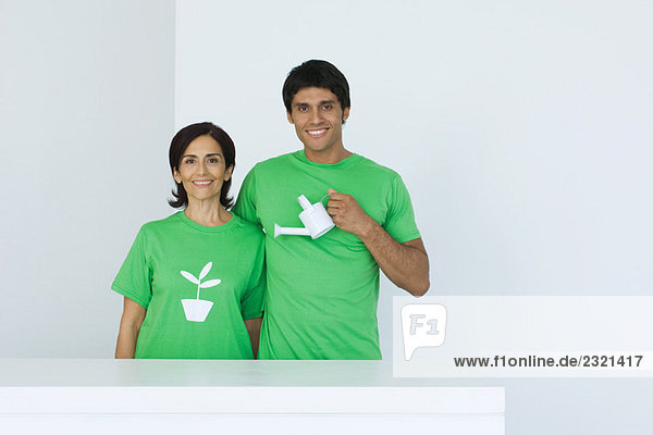 Mann mit Gießkanne  stehend neben Frau mit T-Shirt bedruckt mit Pflanzengrafik  Porträt