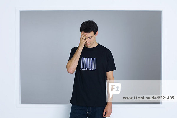 Man wearing tee-shirt printed with bar code  covering face with hand