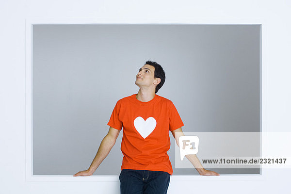 Mann im T-Shirt mit Herzsymbol  aufblickend  lächelnd