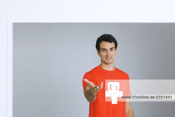 Junger Mann im T-Shirt mit Plus-Symbol  Hand ausstreckend  Kamera lächelnd
