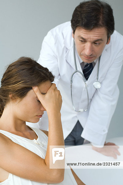 Male doctor examining patient  woman sitting with hand over eyes