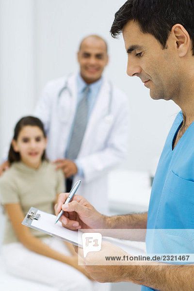 Male nurse writing on clipboard  young patient and doctor in background