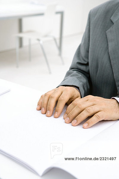 Professioneller Mann am Schreibtisch sitzend  Blindenschrift lesend  abgeschnittene Ansicht der Hände