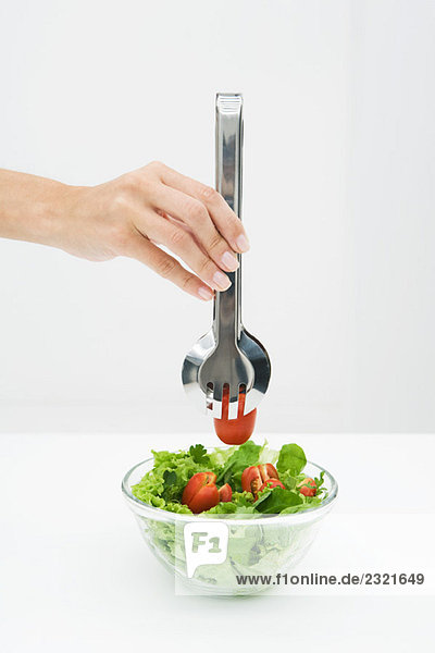 Frau pflückt Tomate aus der Salatschüssel mit der Zange  Blick von Hand geschnitten
