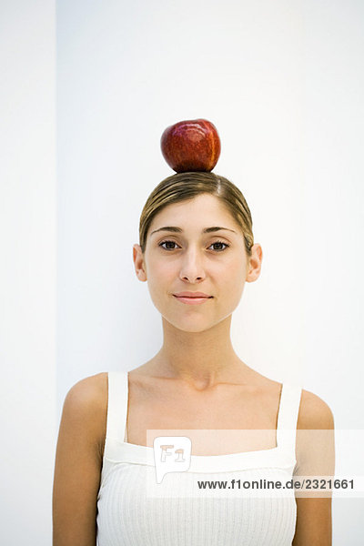 Frau balanciert Apfel auf dem Kopf  lächelt in die Kamera  Porträt